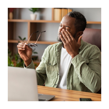 Image of a person sitting at a desk rubbing their face